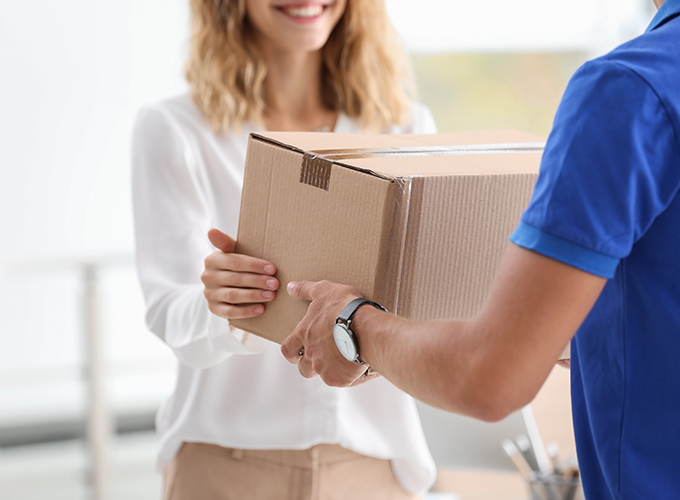 a delivery man in a blue shirt handing a parcel to a smiling lady